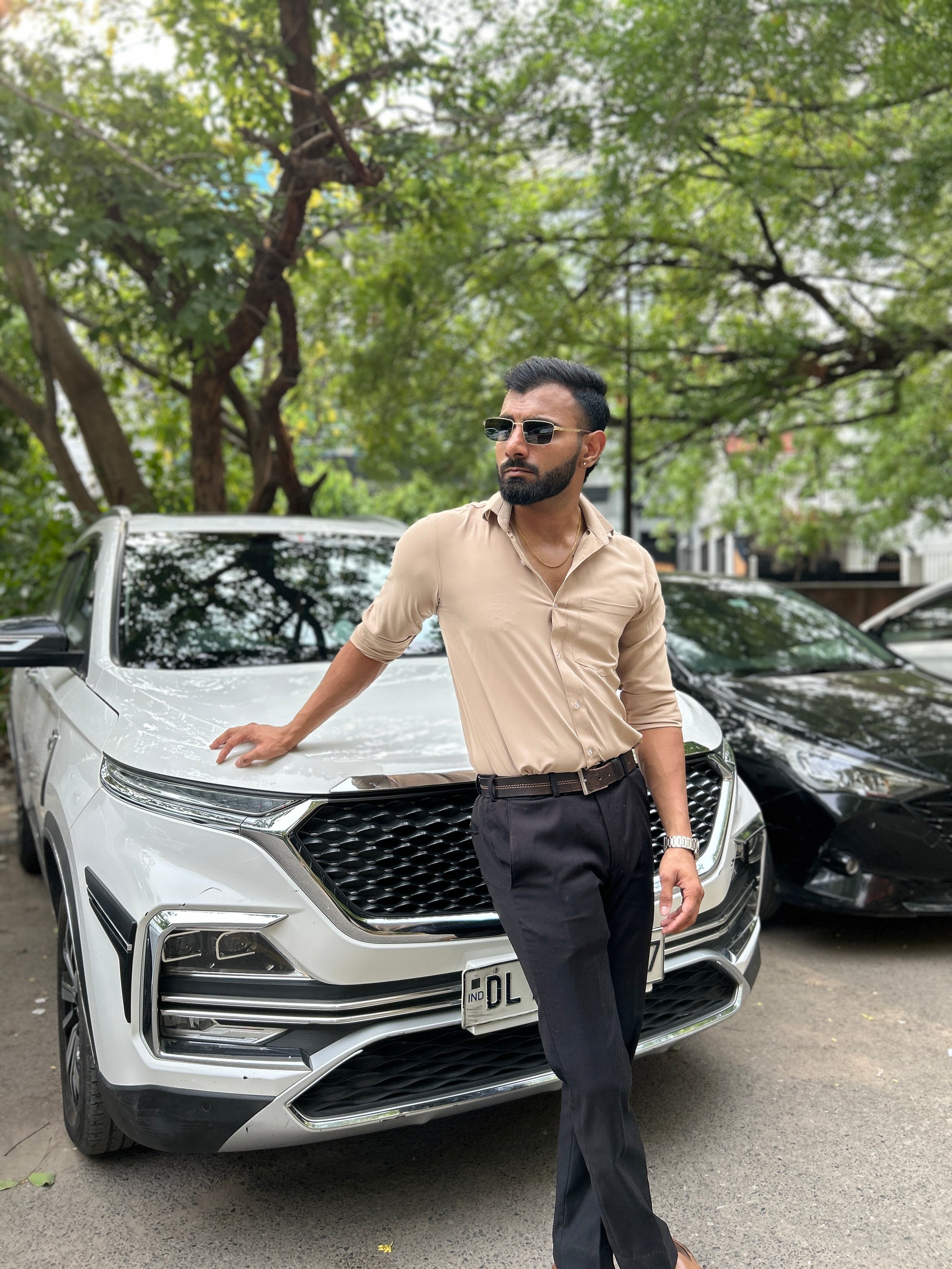Man standing next to a white SUV in an urban setting with trees in the background