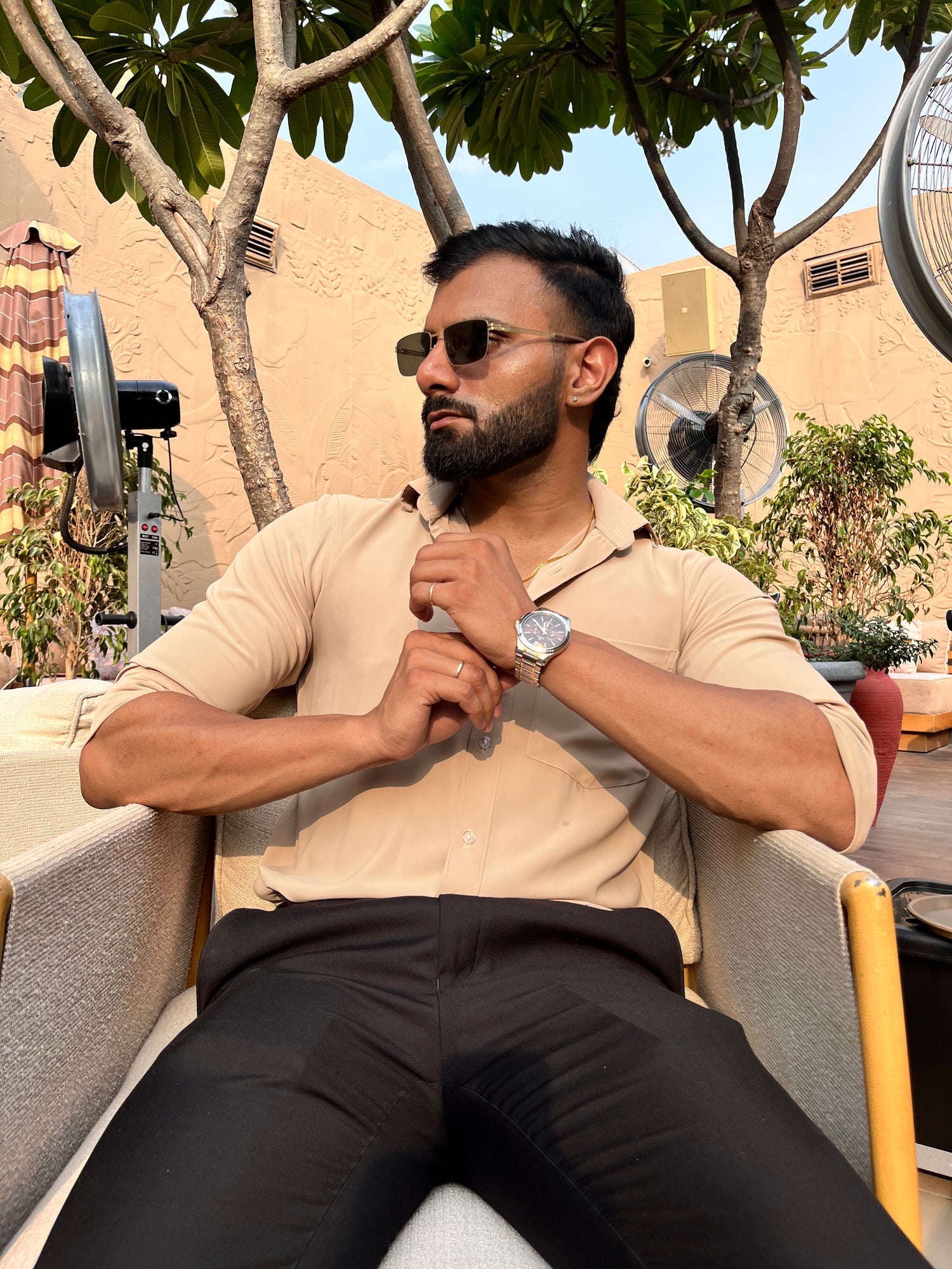 A man sitting outdoors wearing sunglasses and a beige shirt