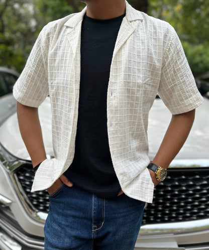 Man wearing a white checkered textured shirt over a black t-shirt with a car in the background