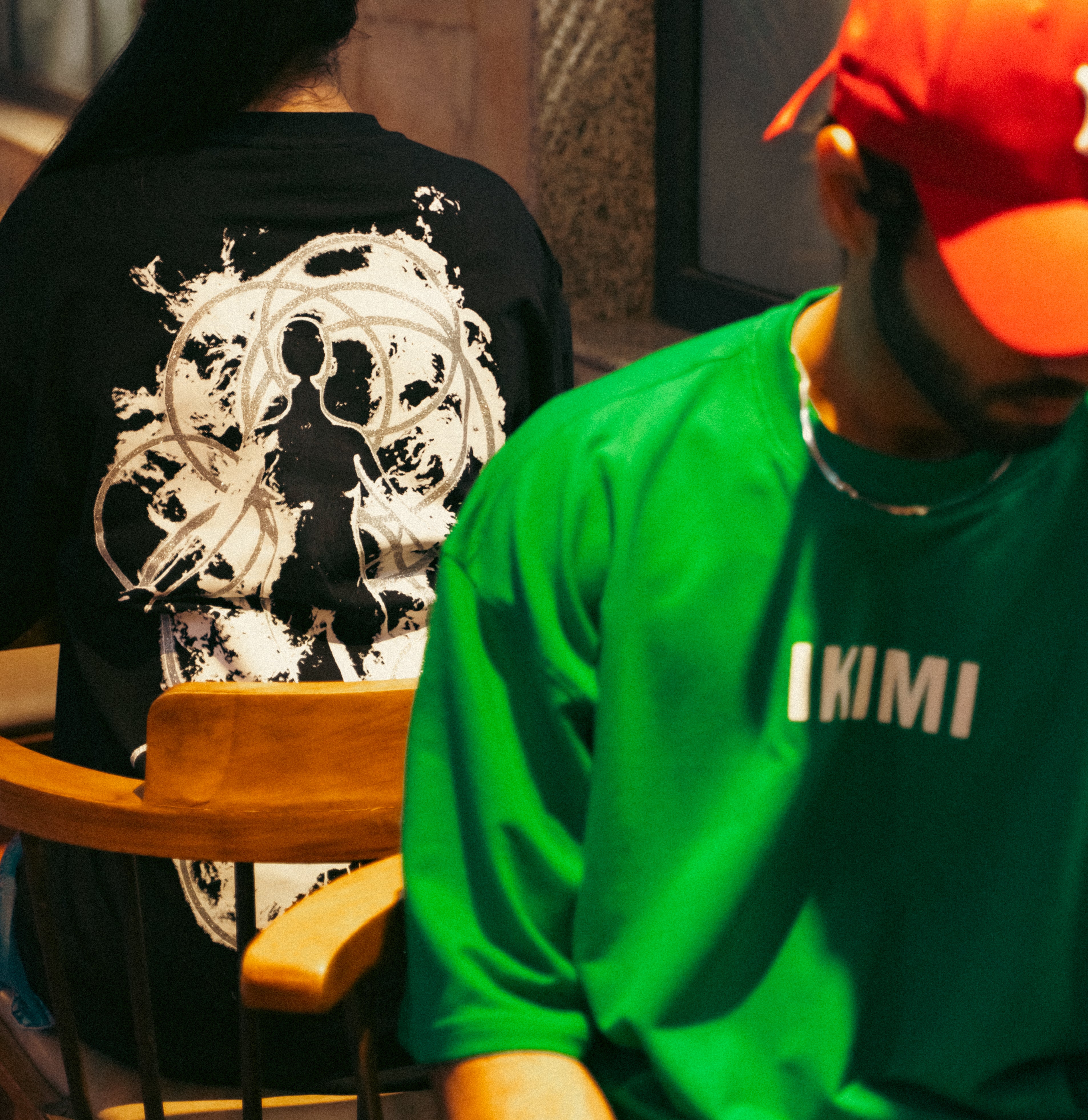 Person wearing a black shirt with a white design and another person in a green shirt with 'IKIMI' text.