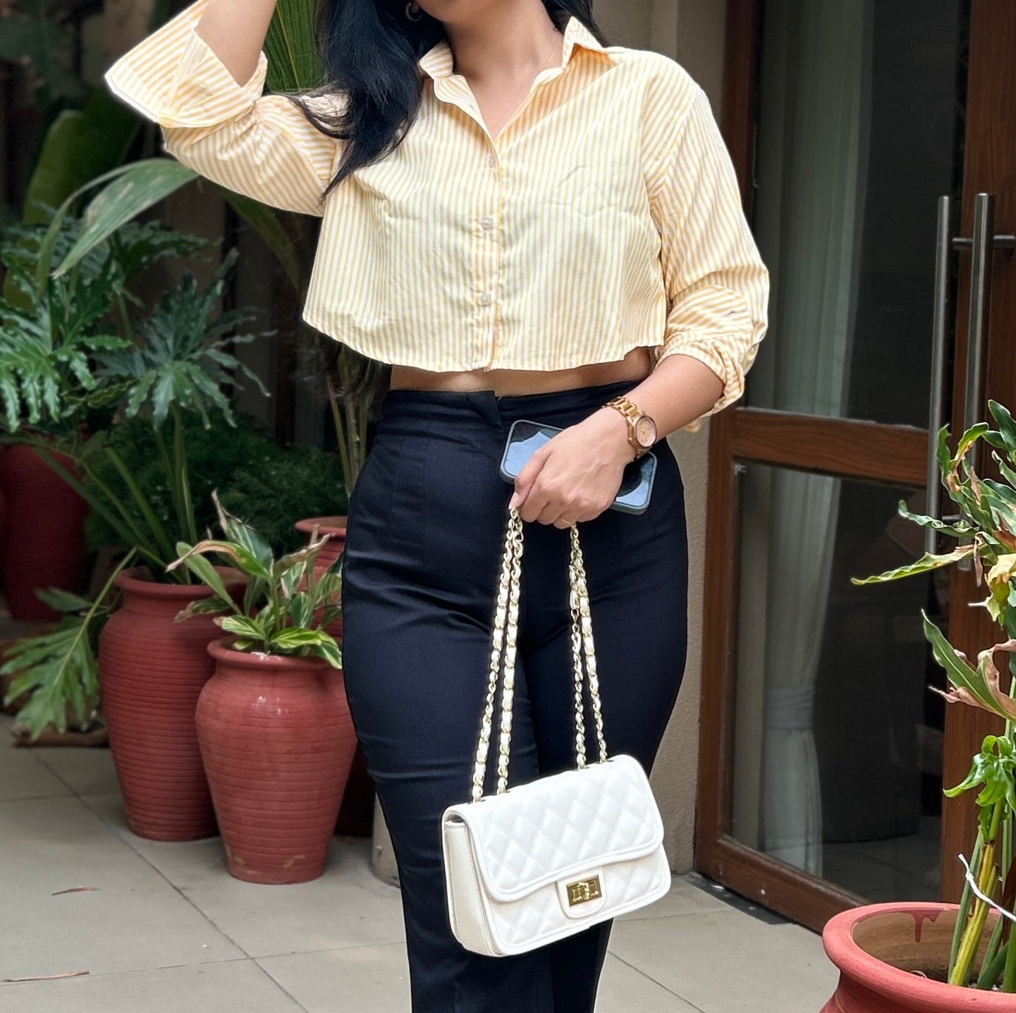 Woman in a yellow crop shirt and black trousers standing in front of a building with potted plants, women blouses, summer shirt for females